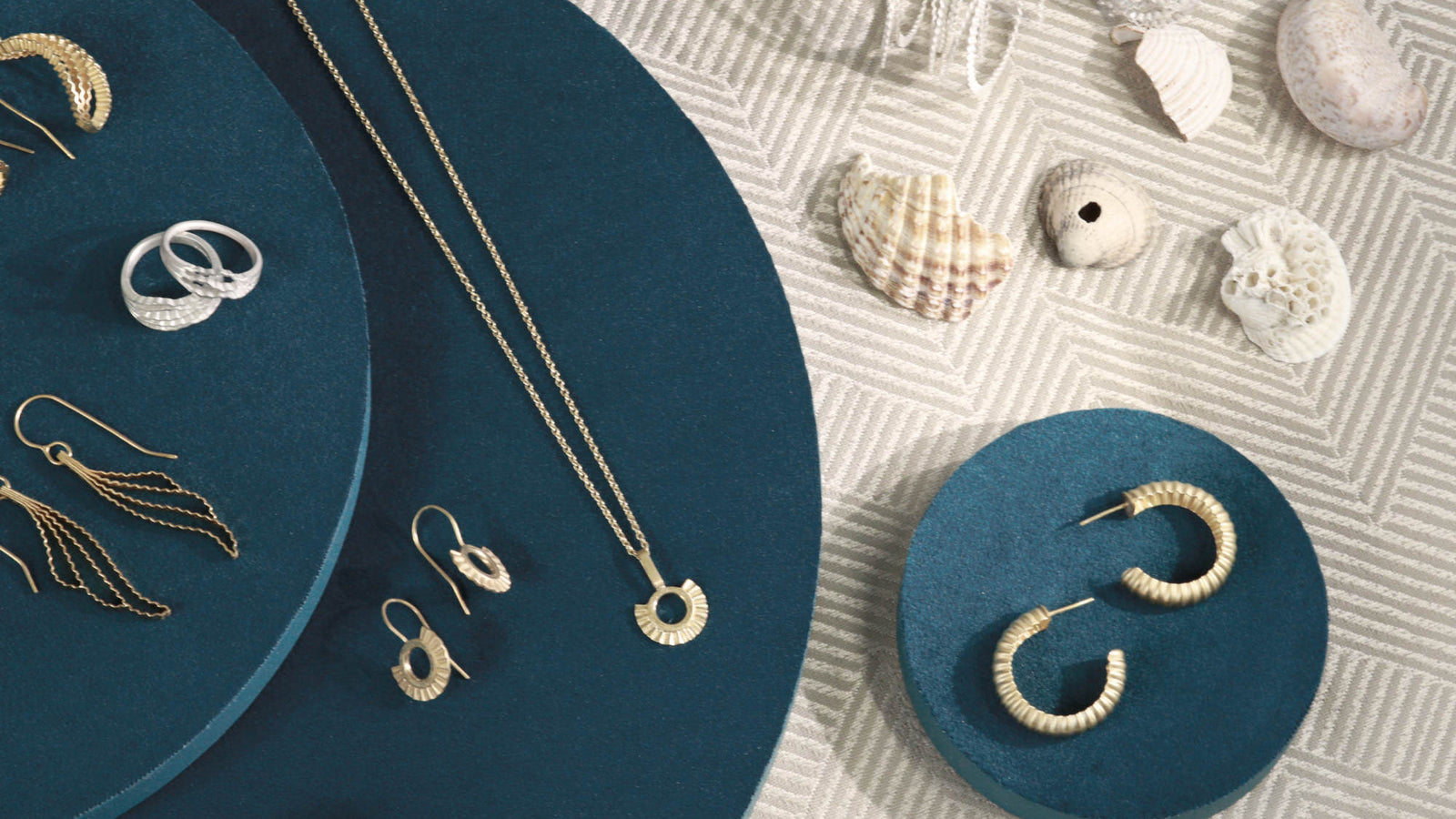Contemporary Handmade Jewelry collection, including earrings and a necklace on a textured surface with seashells.